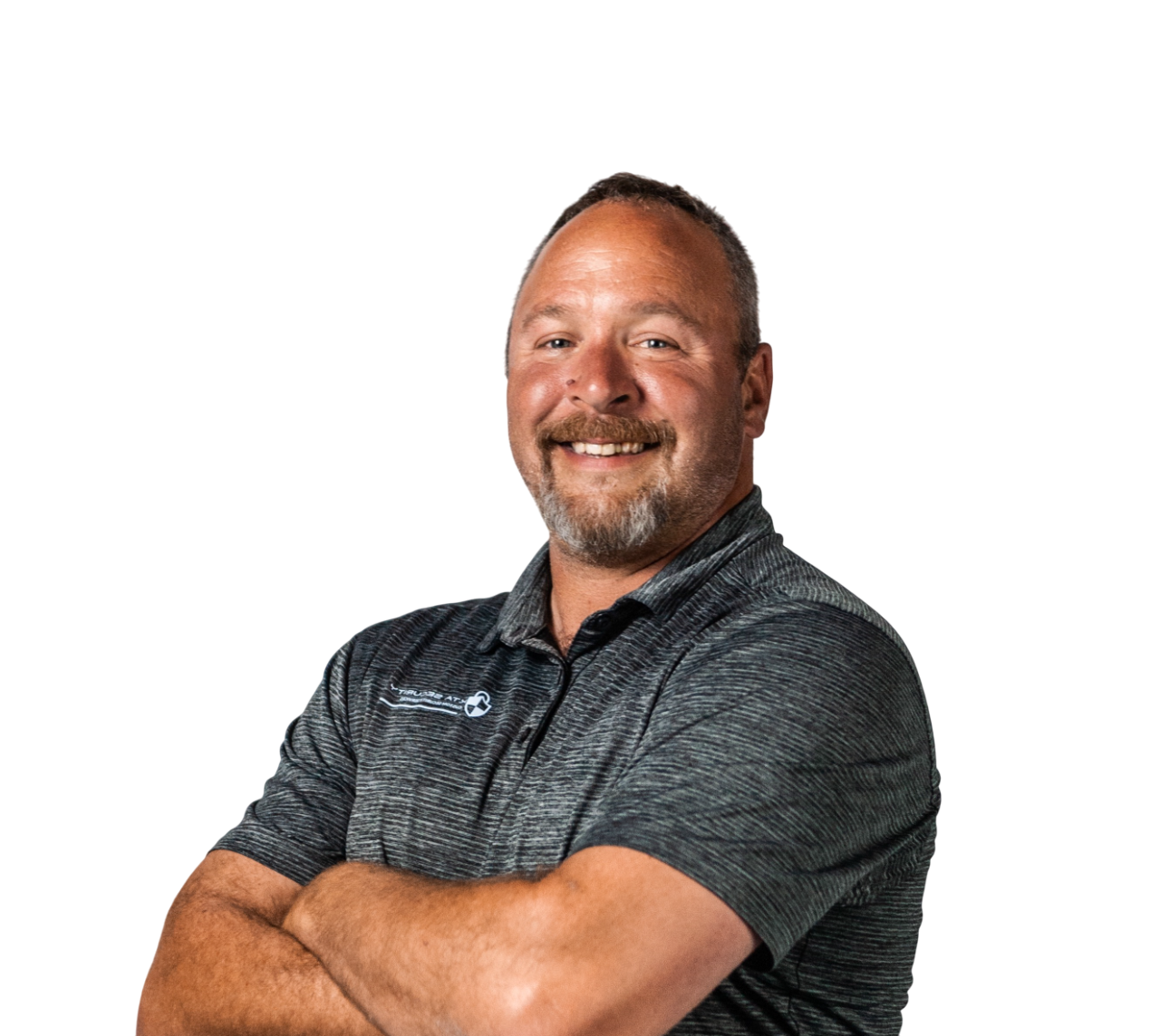 Smiling man with short hair and beard, wearing a gray polo shirt, poses with arms crossed against a black background.