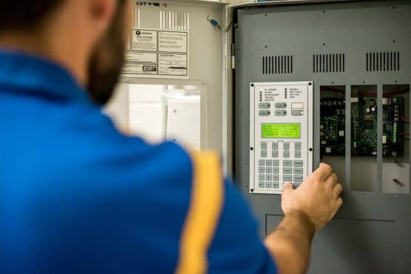 Close-up of a person's hand using a smartphone with a home security app, showing live security camera feeds and control icons for lighting and locks.