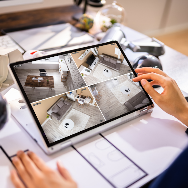 Person viewing four security camera feeds on a laptop screen, showing different interior angles of a room with a couch, table, and chairs.